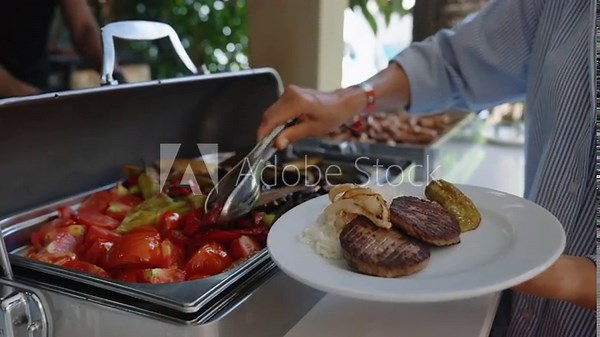 A woman puts food on his plate at a buffet table. All inclusive service. Self Service Catering Buffet. Female hand, woman takes vegan food from heated trays in restaurant, hotel. Close-up.