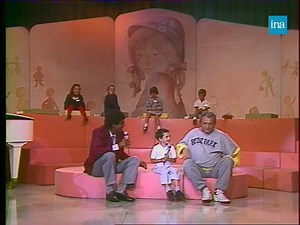 ÉCOLE DES FANS. Alexandre montre qu’il sait faire une galipette, Jacques Martin et Enrico Macias se prêtent à l’exercice. Le chanteur ironise : «On va voir mes pieds noirs !». Alexandre interprète ensuite «Deux ailes et trois plumes». On est en 1984. | INA