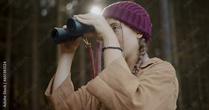 Female explorer observing through binoculars in forest