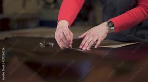 master marks the treated animal skin. He applies and tracks a cardboard template in a small craft workshop