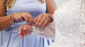 The bride's friend helps her put on the wedding dress by tying the sleeve. Preparation for the wedding ceremony.
