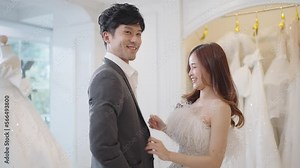 Bride wearing white drees and groom wearing suit choosing and trying on wedding clothing at wedding studio