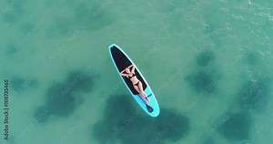 Camera moving around Attractive woman in bikini is sunbathing on a surfboard, aerial view