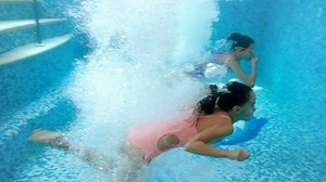 4k footage of two teenage girls holding hands and jumping in swimming pool. View from under the water. Children playing and having fun in pool at gym