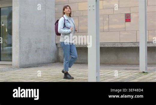 Mid-adult woman with purple backpack entering frame, walking beside wall, checking watch for time. Urban, casual, modern, lifestyle, professional, candid, fashionable Stock Video Footage - Alamy