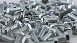 A scattered of stainless M6 threaded bolts. Movement with rotation. Close-up, side view, small depth of field.