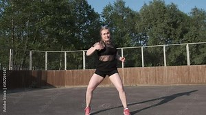young woman dancer in a mesh T-shirt and black short shorts dancing street modern dance, twerking, shaking her buttocks against the background of houses and green trees. Slow motion. Gimbal shot
