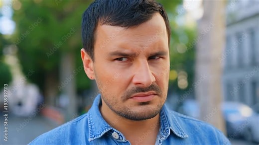 Man looking concerned and suspicious while standing outdoors on a street with trees and buildings, face.