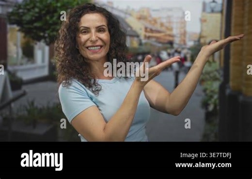 Young hispanic woman smiling gestures open hands on a busy street with blurred buildings; welcome happiness Stock Video Footage - Alamy