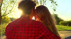 Beautiful happy young couple sitting on the bench in sunny park, kissing and hugging together. Girlfriend and boyfrieng in love, romantic date. Slow motion 240 fps, high speed camera. Full HD 1080p
