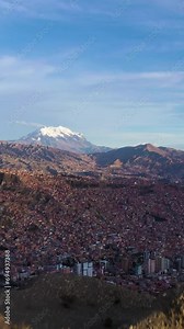 Traveler Hiker Man on Hill Looking at La Paz Cityscape and Illimani Mountain. Beige Rock Formations. Aerial View. Bolivia. Golden Hour. Wide Shot. Establishing Shot. Vertical Video