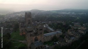 Drone tracks around facade of Durham Cathedral during misty morning twilight. Cathedral lights are still on