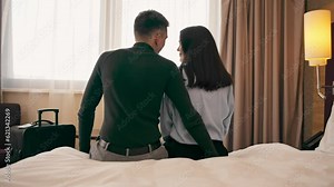 young couple in the room of a luxury hotel room lovers sitting on the bed looking out the window rear view travel concept
