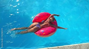 Young millennial woman girl relax in sprinkled doughnut float at swimming pool, has fun during festival, hotel, event smiling with sunglasses on during summer. Beach vacation concept. Top view