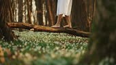 Barefoot woman walks on fallen tree in forest, surrounded by blooming...