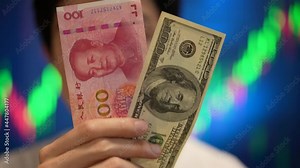 Man holding Chinese Yuan and US Dollar cash in front of stock graph. Finance, trading, trade war and business investment concept b-roll footage. Asian young man holding the money feel happy exciting