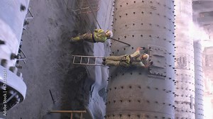 Workers are repairing the grinding mechanism in the workshop of a cement plant. Work technology, cement production. People working in heavy industry. vertical video