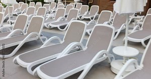 Along pool rows of plastic sun loungers with umbrellas for sunbathers. Empty sun loungers with soft bedding await those who want to relax in sun after swimming
