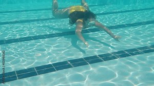 The camera goes down under, there's a girl in a yellow swimsuit and a mask. Swimming pool and camera under water. Slow motion