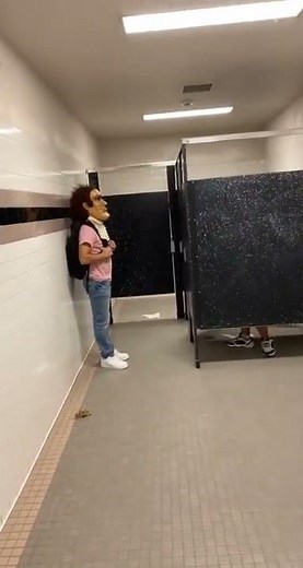 Guy Big Head Mask In Front Of Bathroom Stall