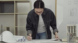 Young Asian female interior architect working with blueprint at the home office.