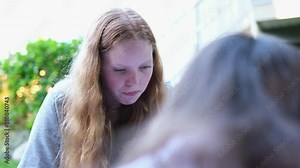 Two young teenage girls play mobile phone play games sit on Internet wi-fi social networks addiction to phones spend time outdoors. eat picnic