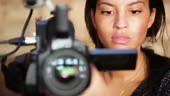 A pretty african american woman operating a high end video camera and...