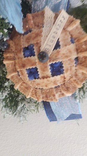 What truly sets this wreath apart is its whimsical blueberry pie charm, nestled perfectly within the design. This unexpected and sweet detail makes it a truly unique piece that will surely spark conversation and bring a smile to all who see it. Blueberry pie from @criss.misswreaths #winterwonderland #winteraesthetic #bluechristmas #christmasdecorations🎄 #flockedwreath #fakebake #blueberries #blueberrypie #jadiantcreations #christmaswreaths | Jadiant Creations