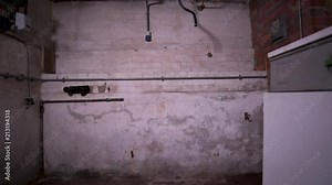 Slider dolly shot inside an old and creepy basement reveals machinery washing machine and dirty and dusty brick walls, copper tubes, pipelines and electric cables.
