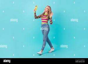 Full length photo of cute cheerful woman dressed striped sweater walking video talking modern gadget isolated turquoise color background Stock Photo - Alamy