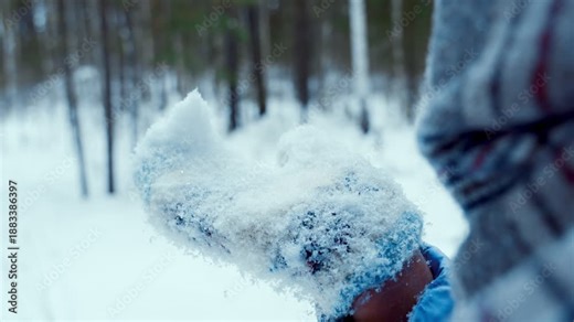 A young girl blows snow off her hands in winter on the street. Snowflakes fly apart. Close-up. People in winter.