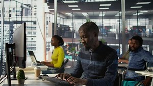 Programmer doing software debugging, asking for help from smiling team leader in wheelchair. Employee fixing coding mistakes, being assisted by cheerful manager with disability, camera B