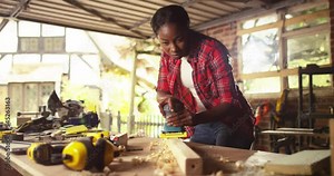 An African American female carpenter and joiner woodworker prepares timber for marking and cutting in her workshop,