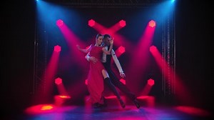 Young couple passionately dancing tango in a dark room with smoke and red spotlights in slow motion.