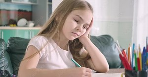 Portrait of tired Caucasian schoolgirl yawning and holding head with hand as sitting at the table. Cute exhausted girl getting asleep while doing homework. Overworking, studying. Cinema 4k ProRes HQ.