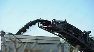 A pavement milling conveyor spewing chunks of asphalt during road construction