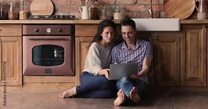 Couple spend weekend relaxing sit on warm wooden floor with underfloor heat system in kitchen using laptop search renovation house design ideas on internet, buy online use e-commerce web site concept