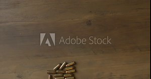 Footage shows how to start loading an empty magazine with both hands on a table top. Individual bullets ammunition are siting on the table and the technique to load is seen. This are NATO 9mm rounds.