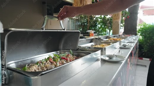 A woman puts food on his plate at a buffet table. All inclusive service. Self Service Catering Buffet. Female hand, woman takes vegan food from heated trays in restaurant, hotel. Close-up.