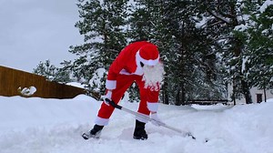 Santa Claus cleans snow with shovel in winter outdoors after a snowfall. Cleaning the streets in the village, clearing the passage for cars, difficult weather conditions for Christmas and New Year