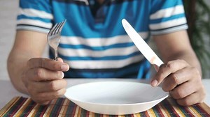 Download Hand holding cutlery with empty plate on wooden table for free