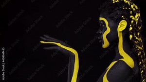 Face art. Woman with black and yellow body paint. Young african girl with colorful bodypaint. An amazing afro american model with yellow makeup.