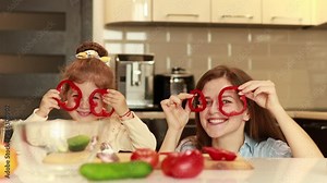 Mother with little daughter cooking together at the kitchen preparing salad