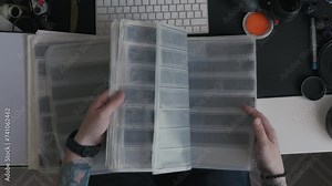 A photographer sits at his desk, intently studying a set of photo negatives, surrounded by the essential tools of his trade