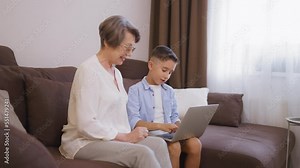 Happy granny learning to use laptop together with little grandson, technology