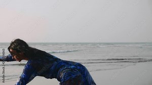 Atmospheric video of young gymnast woman in wet dress doing handspring on sandy beach, close-up in slow motion
