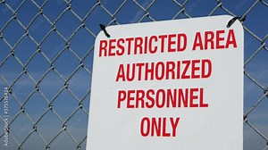 Restricted area, authorized personnel only sign in USA. Red letters, keep off warning on metal fence, United States border symbol. No trespassing notice means violators will be prosecuted by US law.