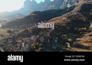 Aerial view flying over a medieval village ruin with stone towers in a vast mountain landscape. Media