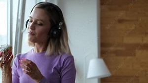 A beautiful girl in a homemade purple suit spends time alone at home. The girl listens to music on headphones, eats sweet cakes and dances, enjoying her vacation. Blonde girl listens to music on