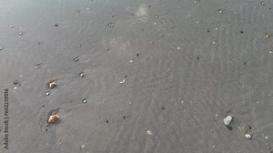 Water flowing over dark sand and small pebbles.